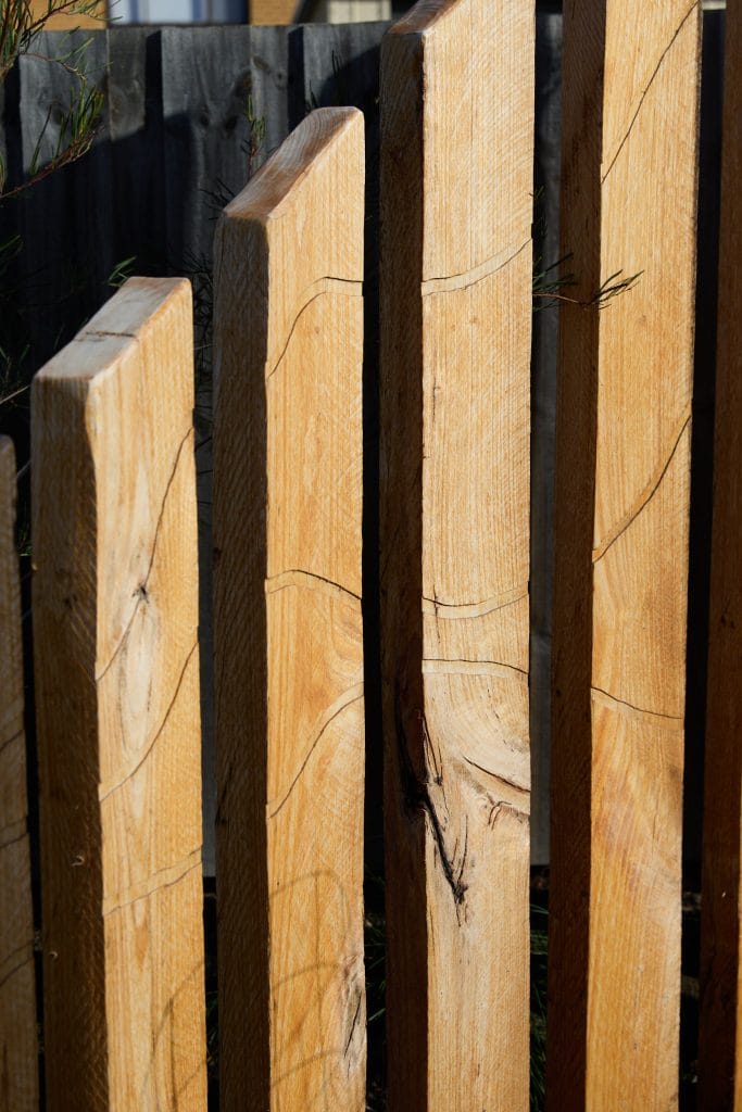 Close-up of vertical wooden fence posts with visible grain and knots, casting shadows. Loci Landscapes | Landscape Designers Tasmania