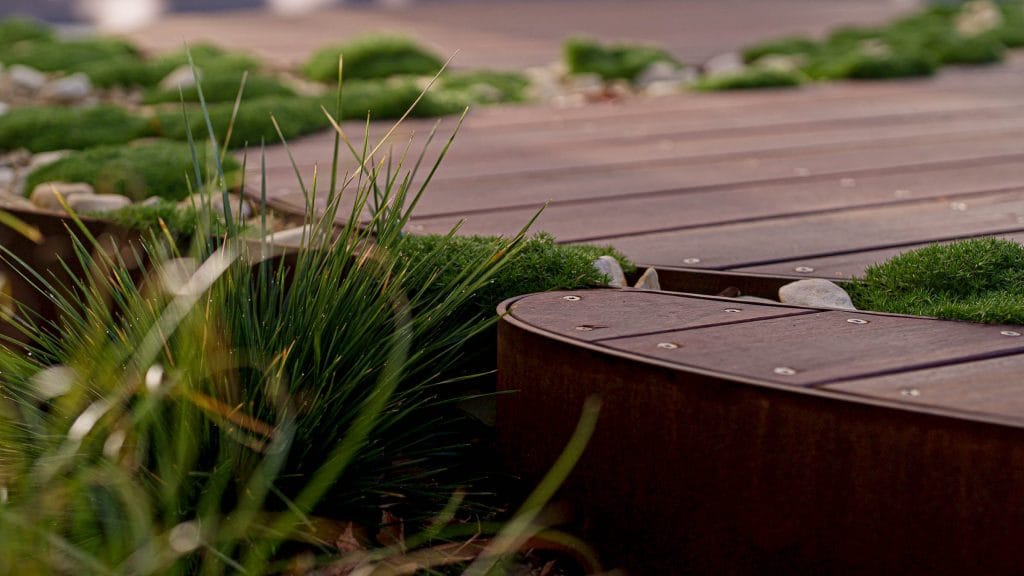 Close-up of a wooden outdoor path bordered by green grass, small plants, and patches of moss. Loci Landscapes | Landscape Designers Tasmania